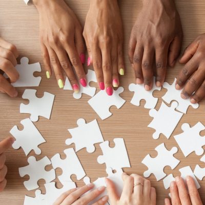 Hands of multi-ethnic business team assembling jigsaw puzzle, to